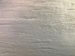 Personne poncant un sol en béton avec une ponceuse, poussière visible dans l'air